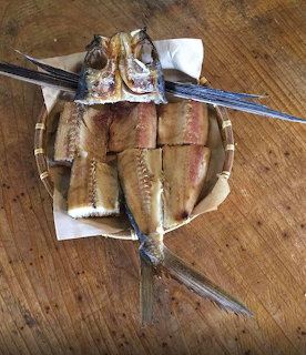 Whole grilled flying fish on a woven tray over white paper on a wooden table