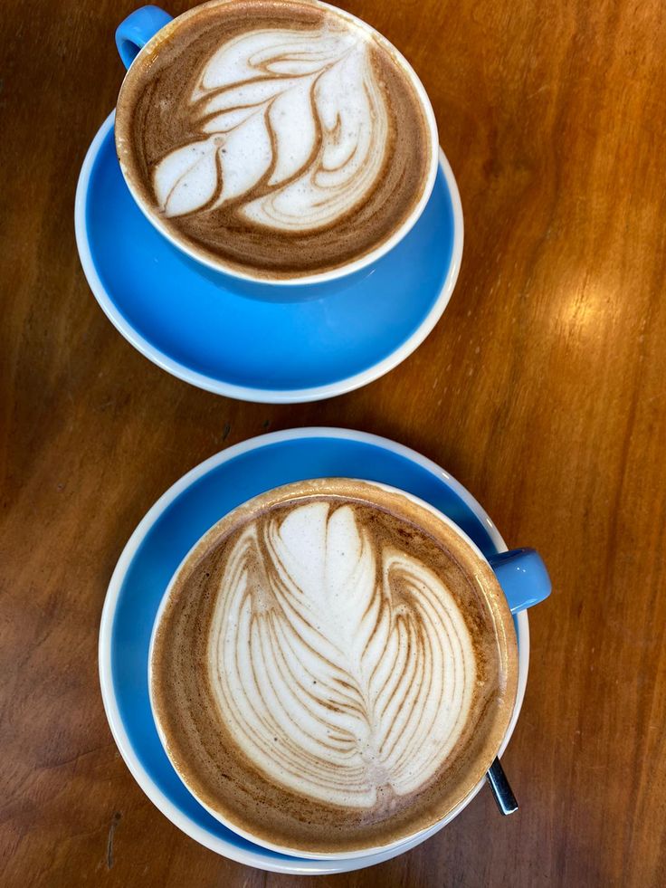 Two blue cups of latte with foam art seen from above on a wooden table