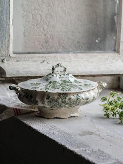 Vintage green floral ceramic lidded tureen on lace near a rustic window