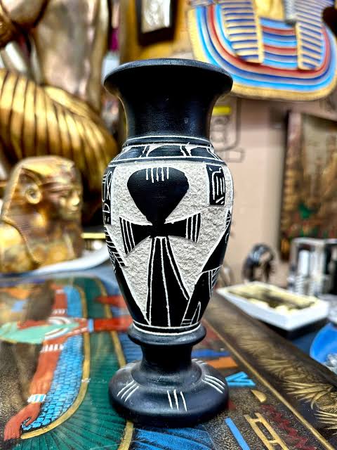 Black vase with white Egyptian geometric designs on display with gold artifacts