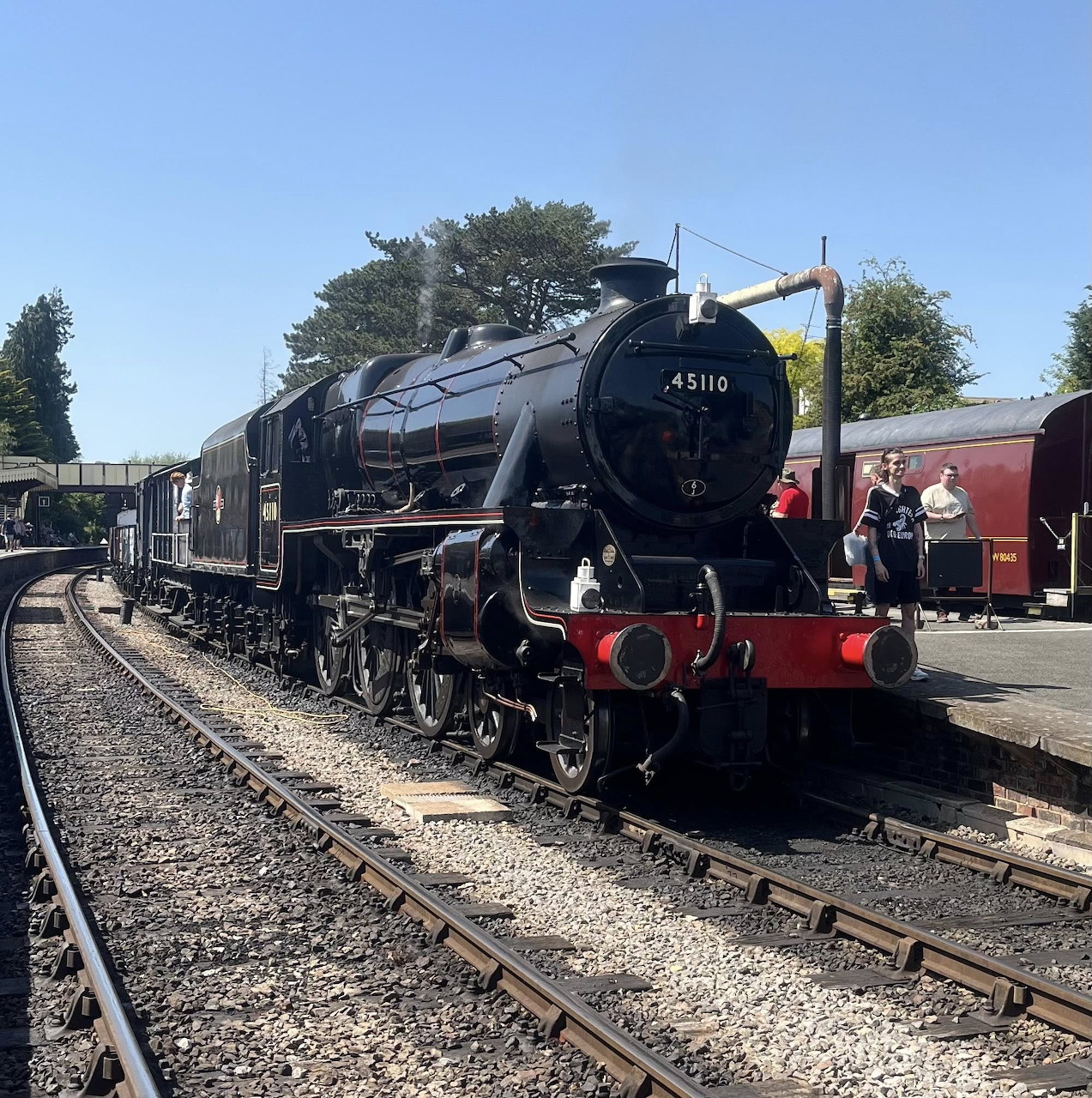 Black steam locomotive 45110 on railway tracks beside a station platform