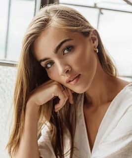 Portrait of woman with blonde hair in white blouse, hand on chin, near window