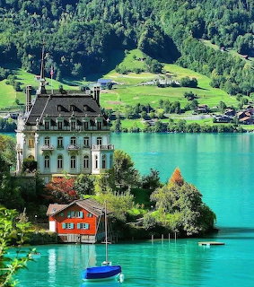 Large lakeside house by a turquoise lake with a small red cottage and a blue boat