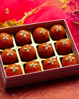 Box of orange Indian ladoo sweets topped with almond slices on a red festive background
