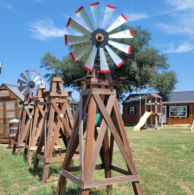 Wooden decorative windmills with red and white blades on tripod stands in a sunny garden setting