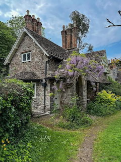 Stone cottage with purple wisteria flowers draped over entrance, garden path and chimney stacks