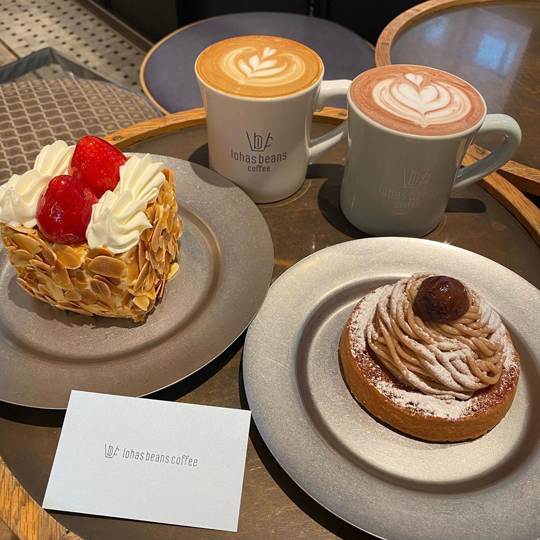 Two coffee cups with latte art, a layered strawberry pastry, and a chocolate-topped swirl tart on gray plates