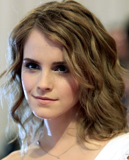 Close-up of a young woman with wavy brown hair and dark eye makeup smiling slightly