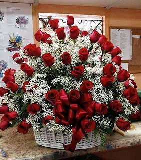 Large arrangement of red roses with baby's breath in a white wicker basket with a red ribbon bow