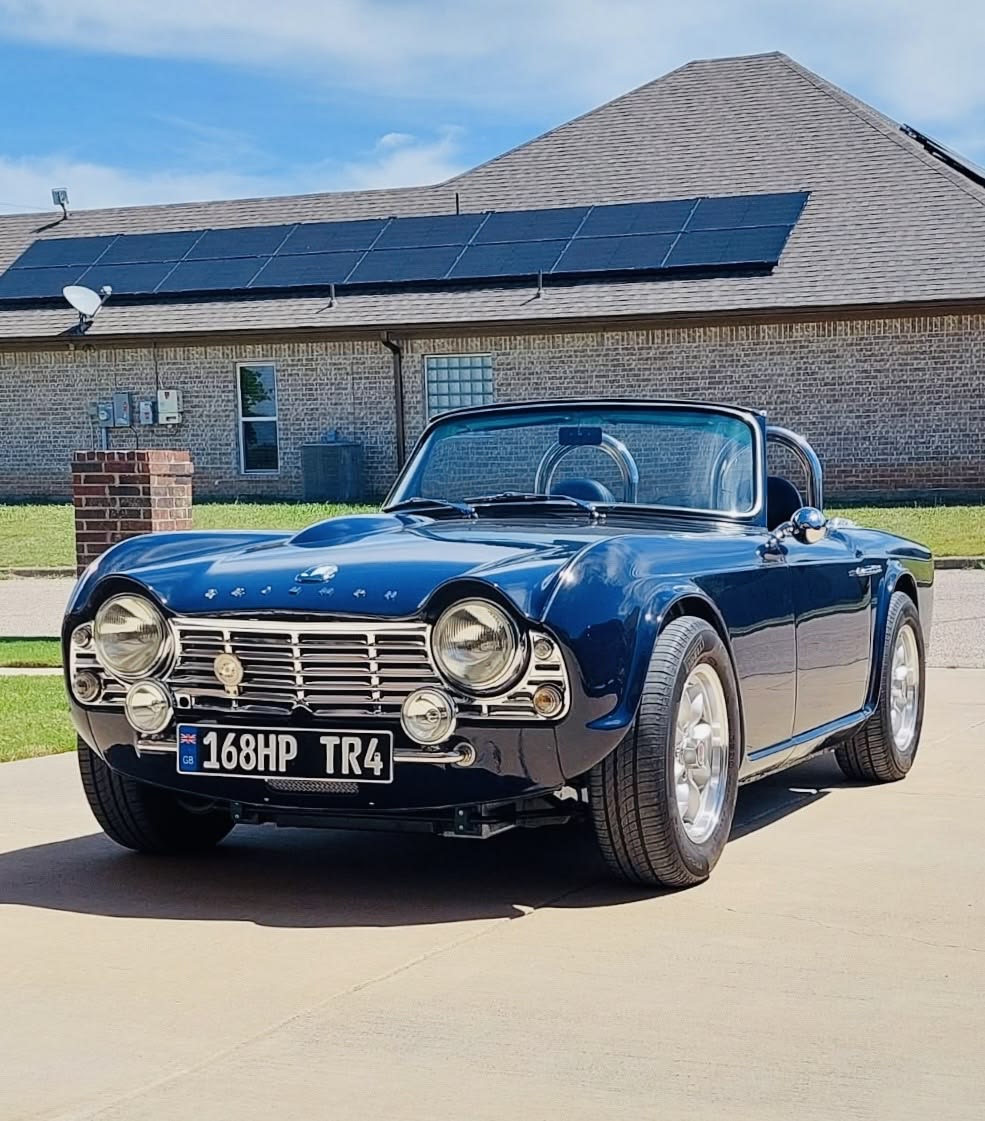 Blue Triumph TR-4 classic convertible sports car parked in front of brick house
