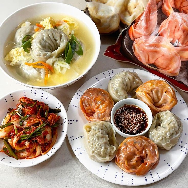 Korean meal with dumplings, kimchi, soup, and steamed buns on white table