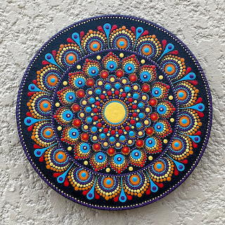Round colorful dot mandala artwork with intricate circular patterns on a textured wall
