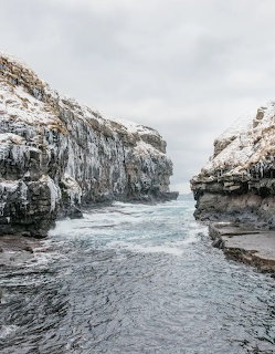 Rocky inlet with steep cliffs on both sides, calm gray ocean water flowing between them under cloudy sky