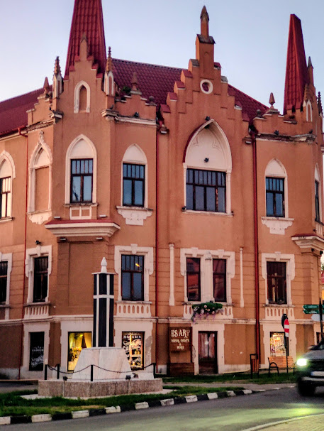 Pink and orange historic building with pointed towers and red roof in Caransebes at twilight