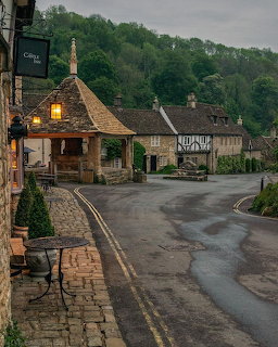 Curving village road lined with old stone cottages beneath a green hillside