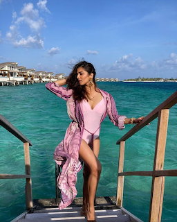 Woman in pink swimsuit posing on wooden dock over clear turquoise water with overwater bungalows behind