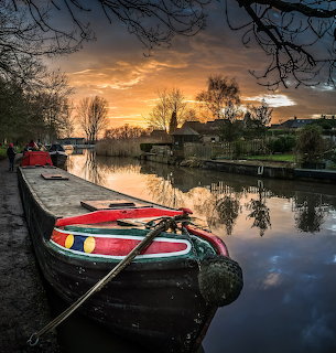 Colorful canal boats moored at sunset with orange sky and reflections in calm water