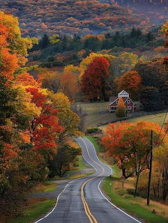 Scenic winding road through vibrant fall foliage in Vermont mountains with small white church