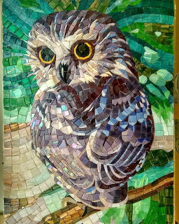 Mosaic art of an owl with yellow eyes perched on a branch made from colorful glass tiles
