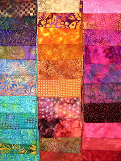 Patchwork grid of colorful batik fabric squares with patterns and tie-dye in blue, pink, orange, and purple tones