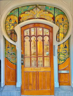 Ornate Art Nouveau doorway with stained glass, wooden door, and decorative tile work in turquoise and gold