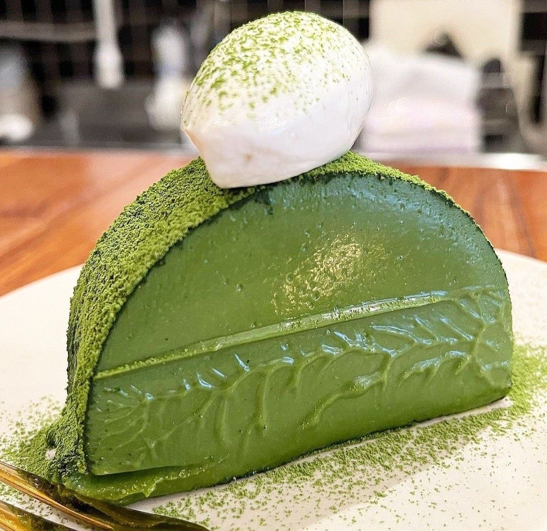 Green matcha mousse dessert with white chocolate dome topped with matcha powder on wooden surface