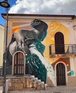 Surreal street art mural painted across the facade of an old building in Quaglietta, Italy