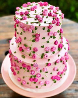 Three-tier white cake decorated with pink roses and green leaves on pink stand