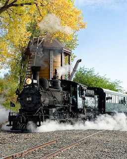 Black steam locomotive 961 puffing steam on tracks with yellow autumn trees