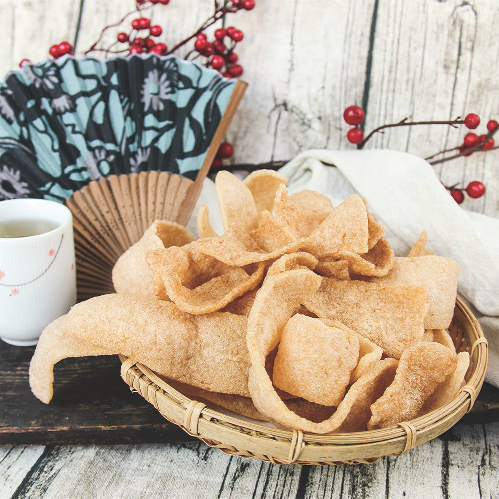 Basket of crispy shrimp crackers on a wooden table with a teacup and decorative fan