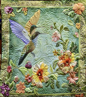 Quilted fabric art with hummingbird and flowers on mint green background with decorative border