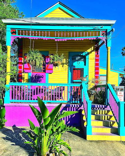 Brightly painted multicolored house with yellow walls, pink accents, turquoise porch railings, and tropical plants