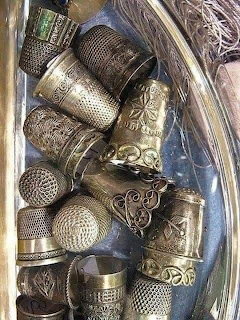 Close-up of assorted engraved metal thimbles in a glass dish
