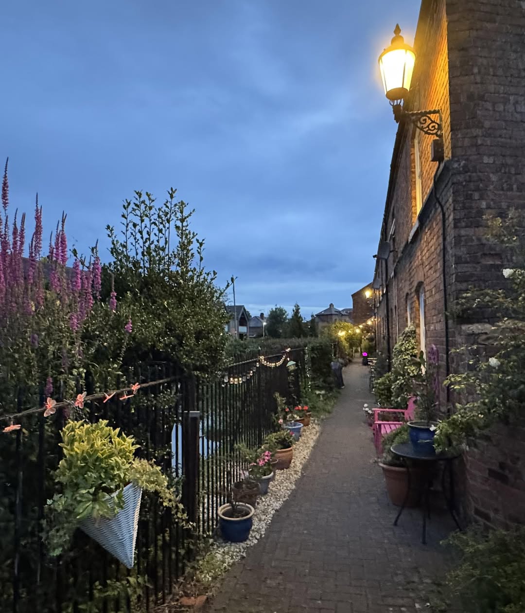 Stone cottage with lamp and garden path at dusk with purple and yellow flowers