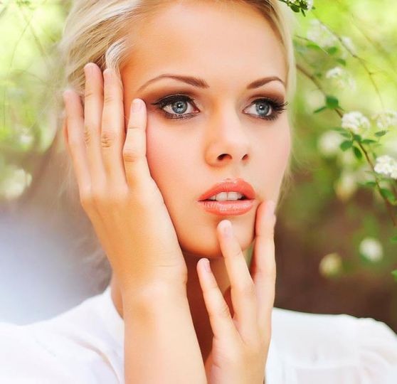 Close-up portrait of a blonde woman touching her face with a soft green blurred background
