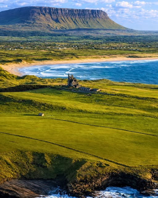 Classiebawn Castle in green coastal fields with a sandy bay and flat-topped mountain in the background