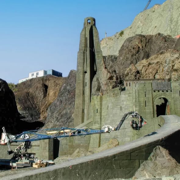Stone fortress tower and wall on a rocky hillside beneath a blue sky