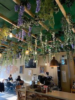 Café interior with hanging purple flowers and plants from wooden ceiling beams, tables and patrons below