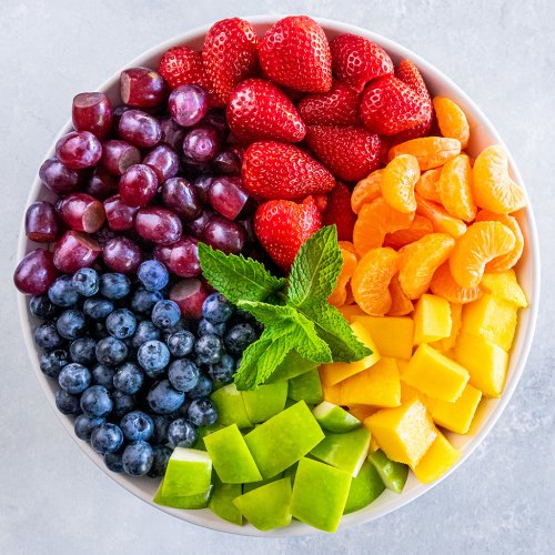 Circular white platter with fresh fruit arranged in rainbow color sections with mint garnish in center