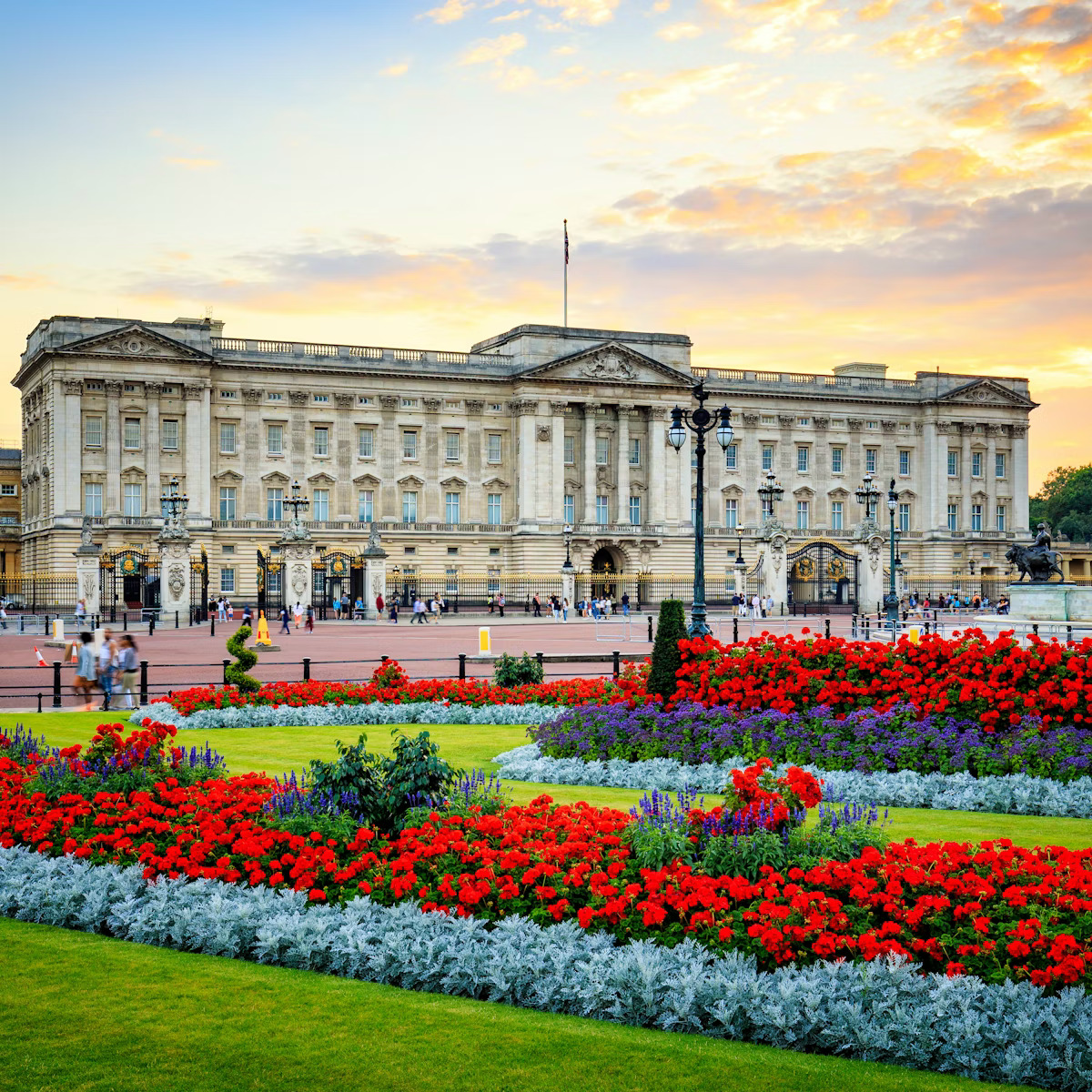 Buckingham Palace with vibrant red and white flower beds in front under sunset sky