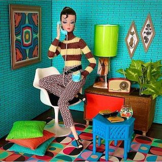 Fashion doll seated in a colorful retro room with bright furniture, patterned floor, and plants