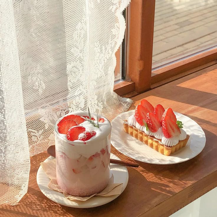 Strawberry latte and strawberry tart on a sunlit wooden windowsill by a lace curtain