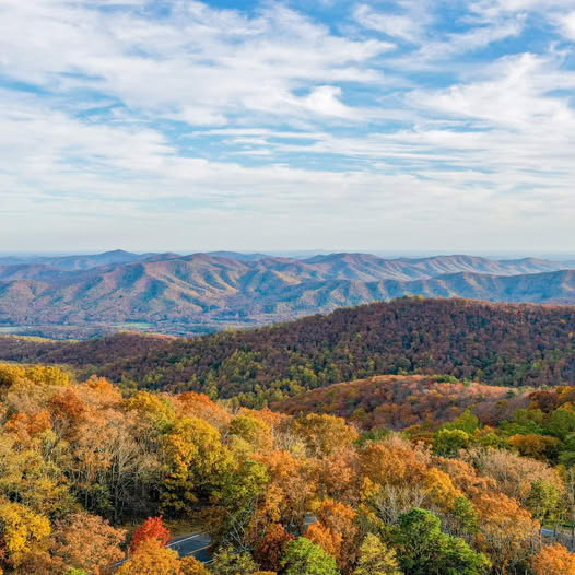 Panoramic view of Appalachian mountains covered in colorful autumn foliage under a blue sky with clouds.