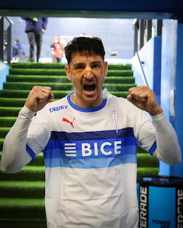 Fernando Zampedri celebrating in a white and blue soccer jersey on green stadium steps