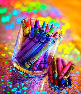 Colorful crayons standing upright in a glass cup with rainbow bokeh background and scattered glitter