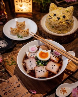 Kawaii cat-faced ramen bowl with pork and egg, alongside cat-shaped rice and small cat onigiri on wooden table
