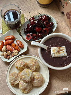Overhead view of Korean food including dumplings, red bean soup, cherries, dates, and a drink on a table