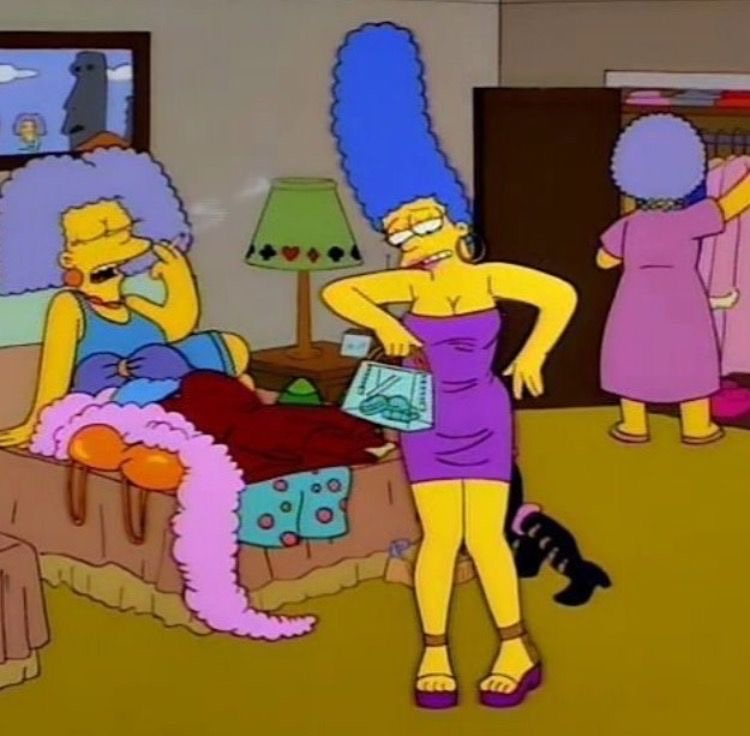 Marge Simpson standing in living room with family on couch in background