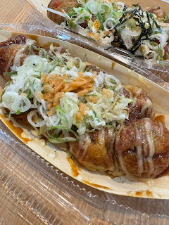 Takoyaki in a tray topped with sauce, mayonnaise, tempura flakes, and chopped scallions