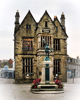 Historic gothic stone building with pointed gables and a bronze statue with flower planters in front